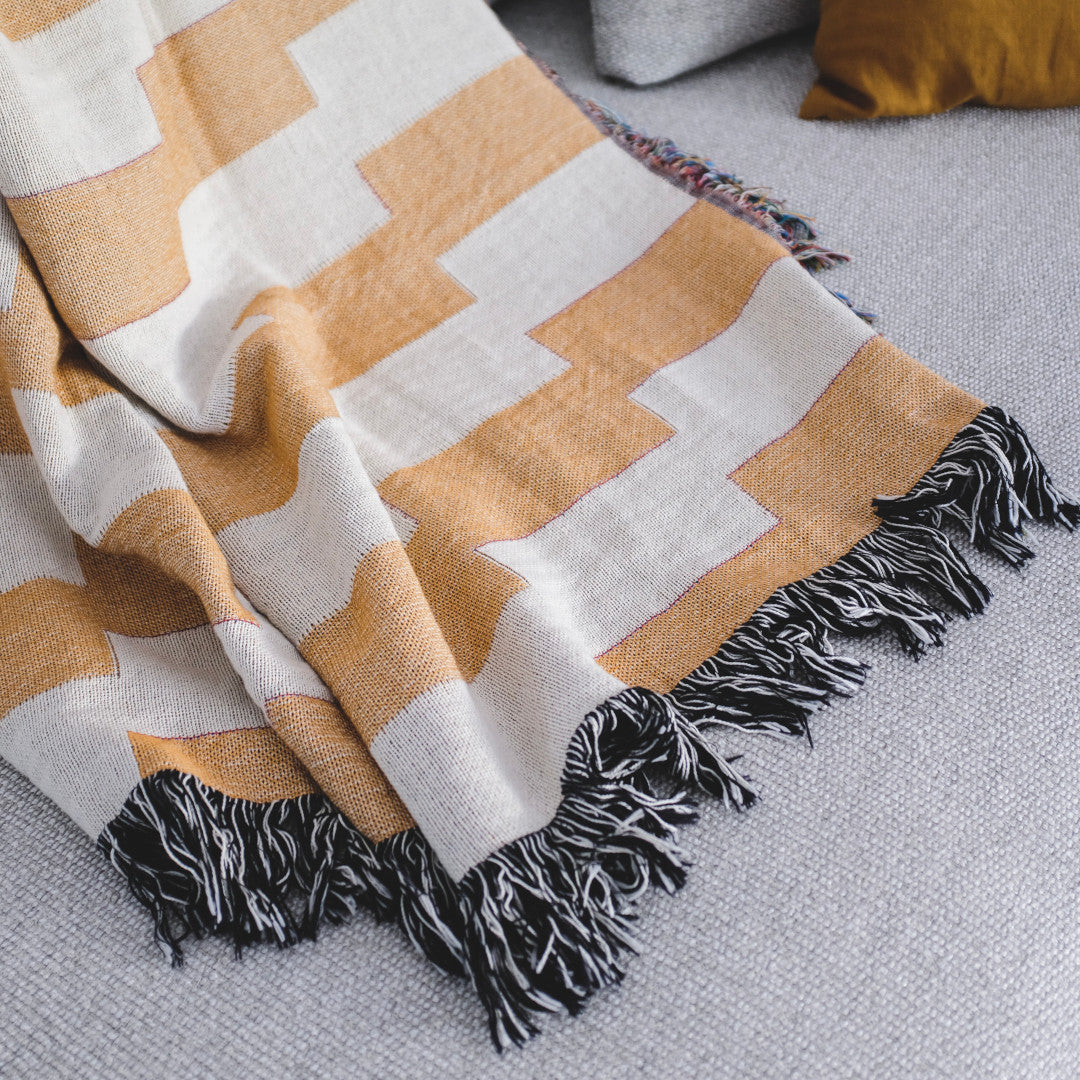 The Amalfi Club orange and white striped woven throw blanket laid on a light grey couch.