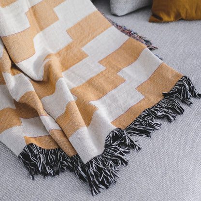 The Amalfi Club orange and white striped woven throw blanket laid on a light grey couch.