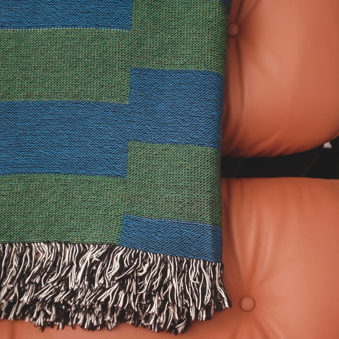 The Capri Club green and blue striped woven throw blanket laid on a brown leather chair.