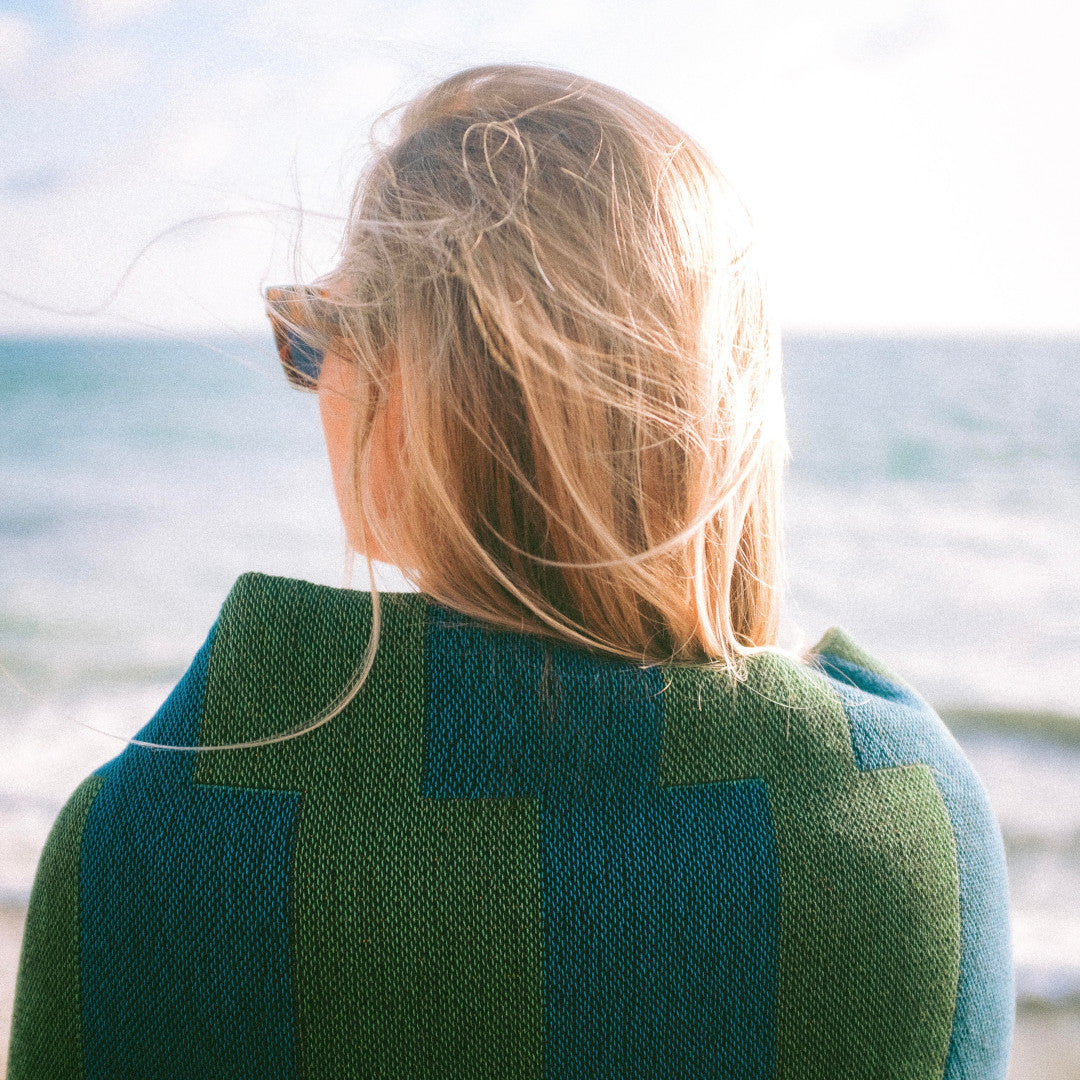 The Capri Club green and blue striped woven throw blanket wrapped around girl with blonde hair while at the beach.