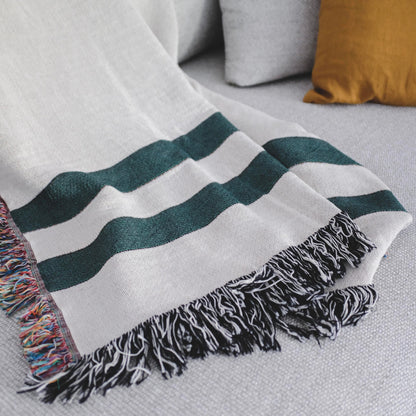 The Fletcher Stripes white with green striped woven throw blanket laid on a light grey couch.