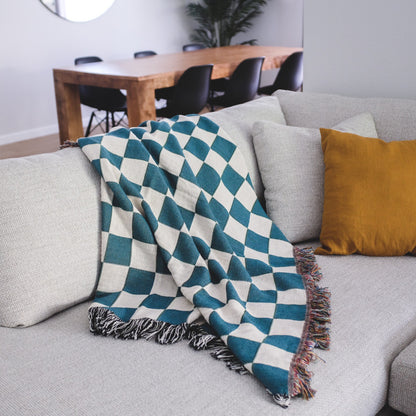 The Solana Checkered teal and white checkered woven throw blanket laid on a light grey couch.