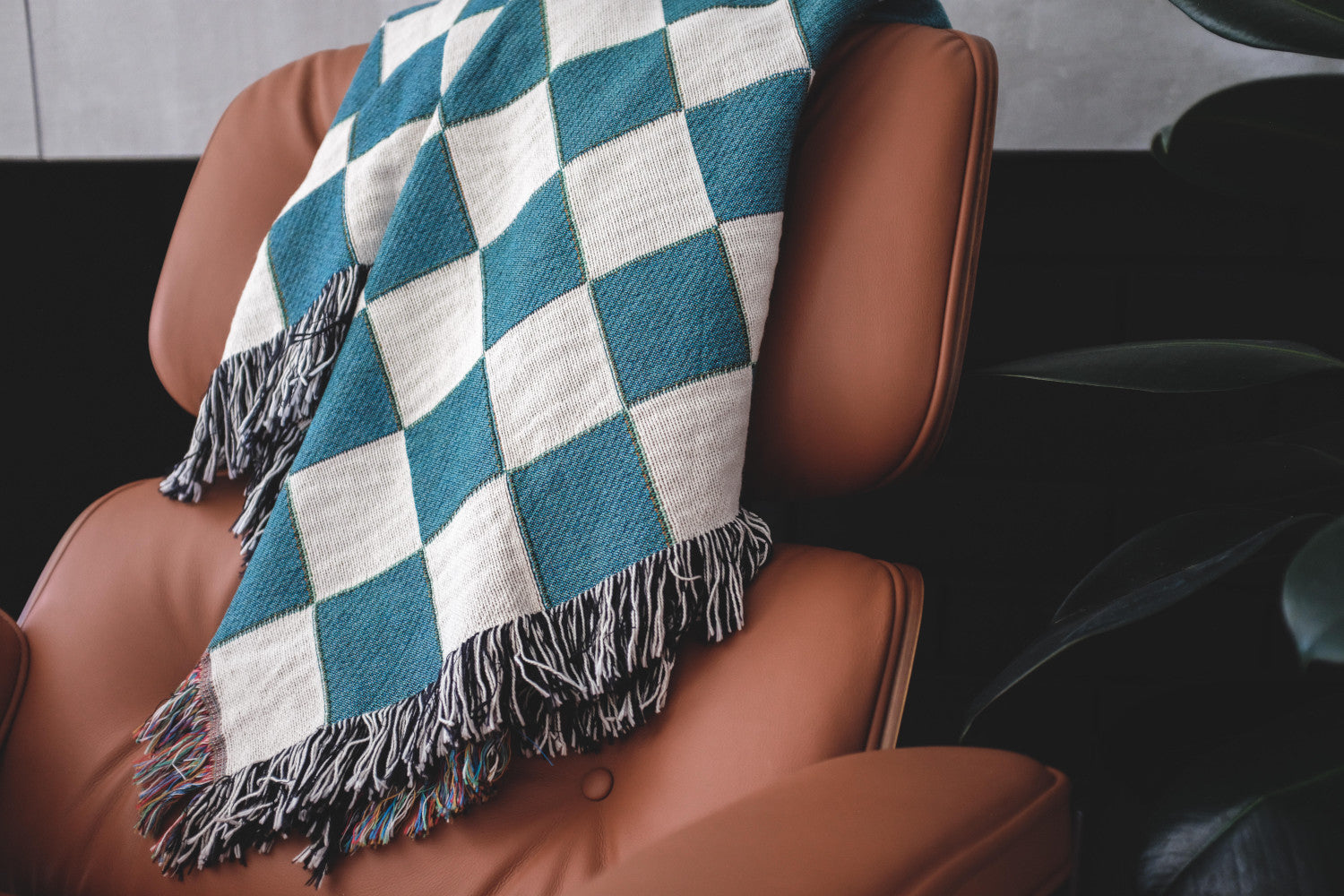 The Solana Checkered teal and white checkered woven throw blanket laid on a brown leather chair.