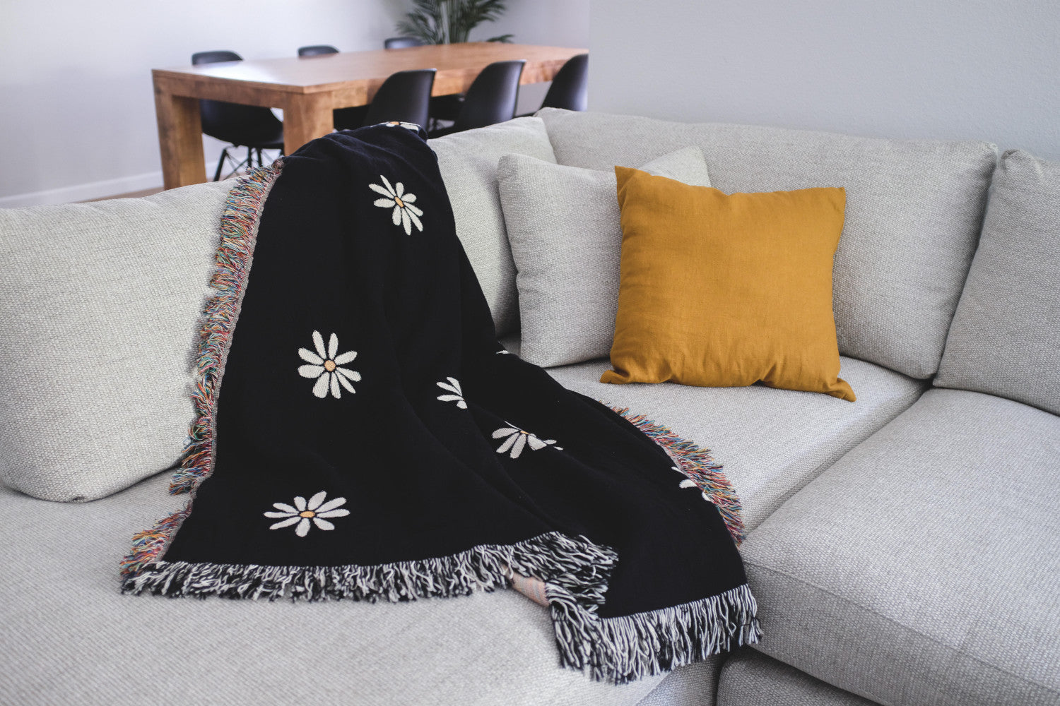 The Superbloom black with white flowers woven throw blanket laid on a light grey couch.