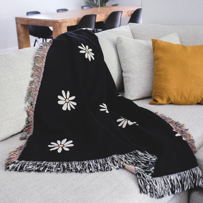 The Superbloom black with white flowers woven throw blanket laid on a light grey couch.